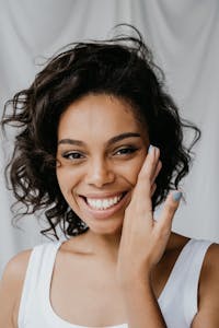A cheerful woman with curly hair and a radiant smile in a close-up portrait indoors.