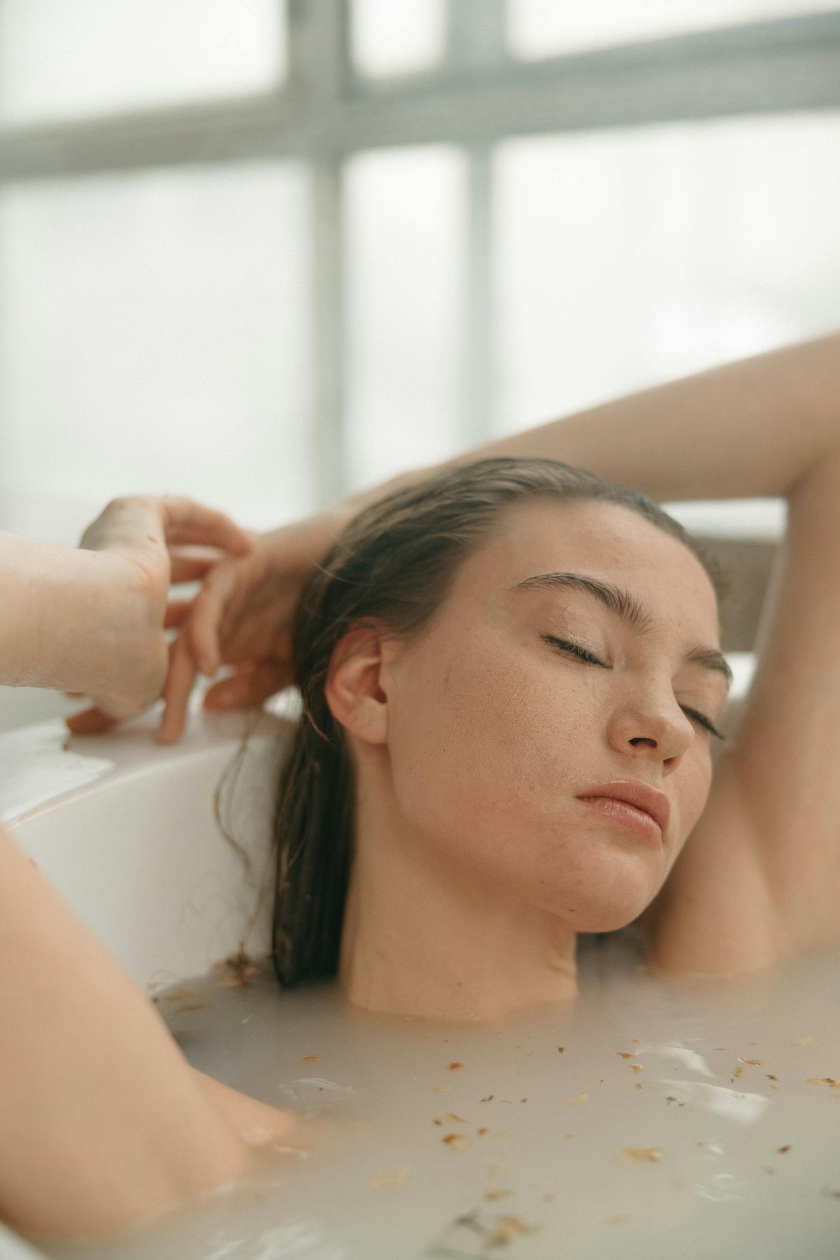 A serene woman relaxes in a milky bath, eyes closed, conveying peacefulness.