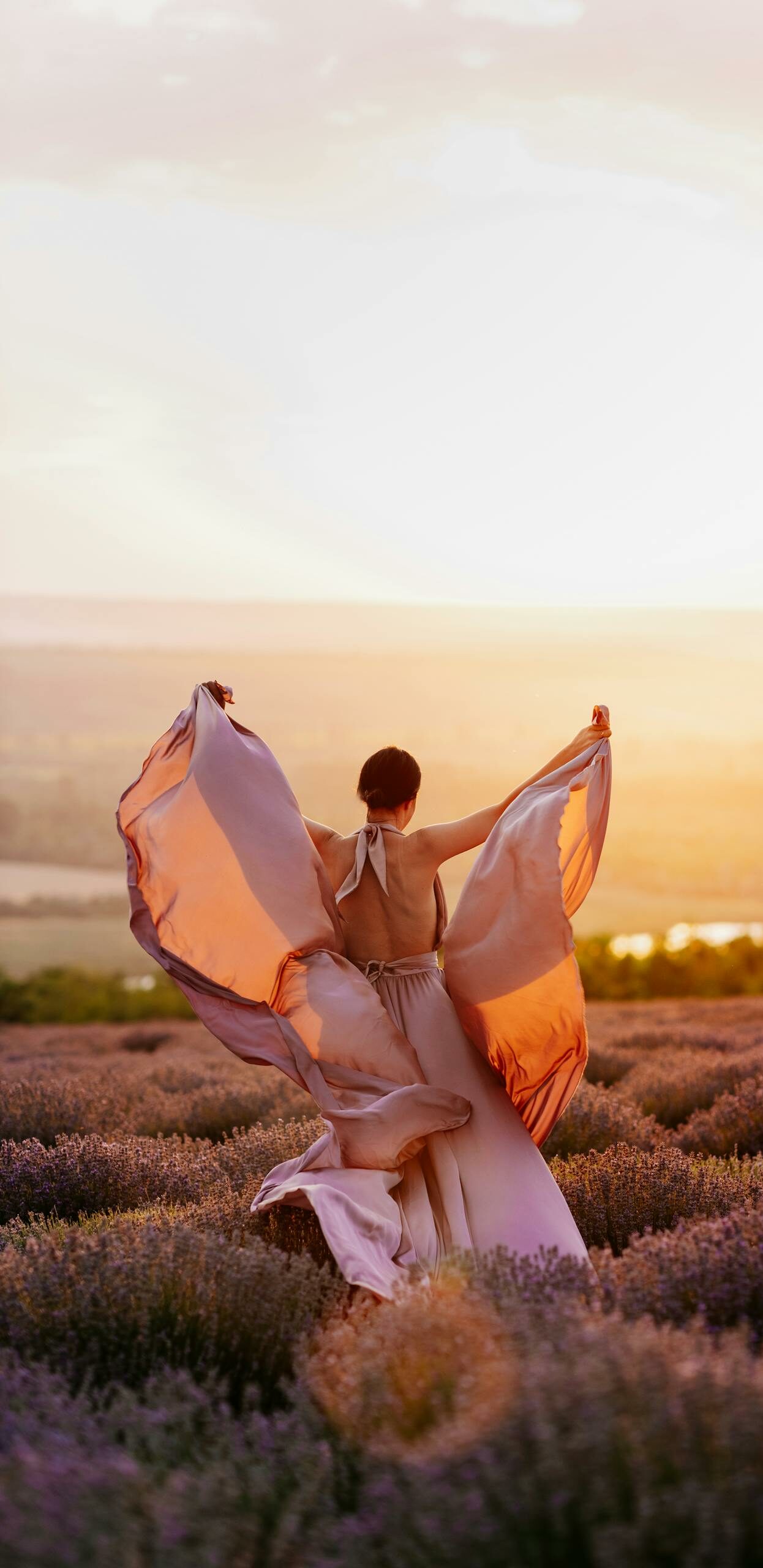 A woman in a flowing dress dances through a lavender field at sunset, embracing nature.