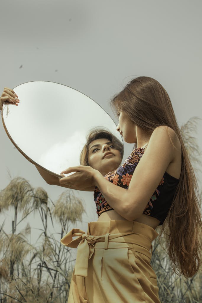Woman in floral top standing outdoors holding a mirror with reflection.